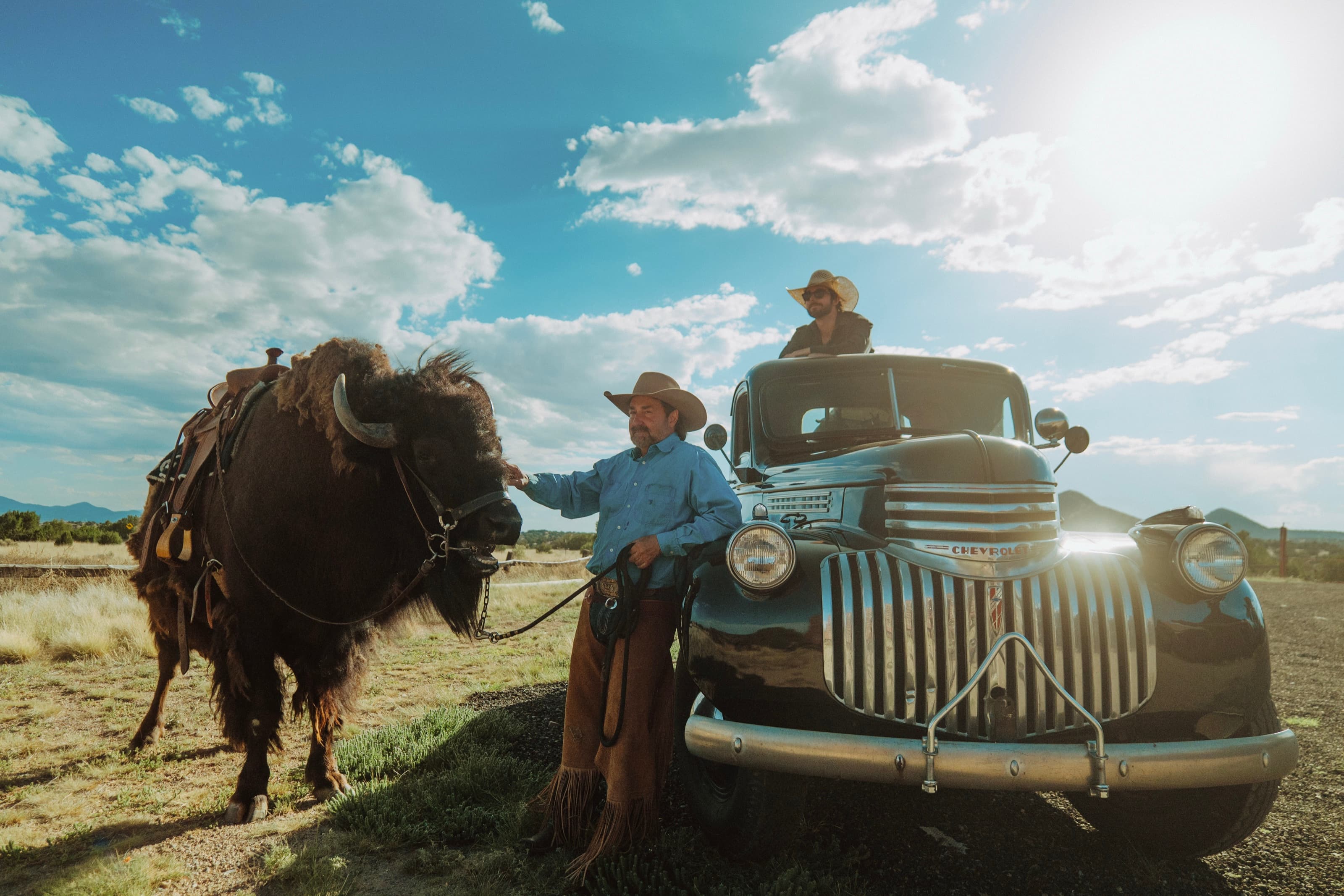 A cowboy with Clyde the buffalo beside a vintage pickup at Mortenson Ranch outside Santa Fe